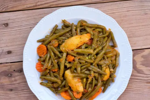 Ein Teller mit einem köstlichen Fasolakia Rezept, das grüne Bohnen, Kartoffeln und Karotten in einer würzigen Sauce zeigt.