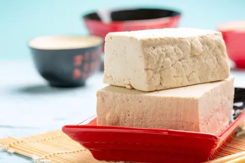 Zwei Blöcke Tofu auf einem roten Teller, bereit zum Genuss. Ja, man kann Tofu roh essen, er ist vielseitig!