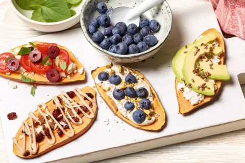 Brotalternativen: Süßkartoffelscheiben belegt mit Tomaten, Feta, Oliven, Blaubeeren, Pistazien, Avocado und Leinsamen.
