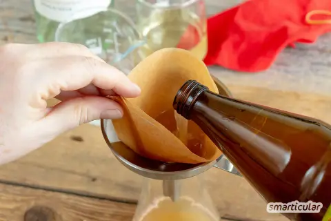 Flüssigkeit wird aus einer braunen Flasche durch einen Kaffeefilter in ein Glas gegossen. So gelingt essig selber machen.