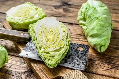 Frischer Spitzkohl, halbiert und auf einem Holzbrett mit einem Hackmesser. Perfekt, um Spitzkohl roh zu essen für einen knackigen Salat.