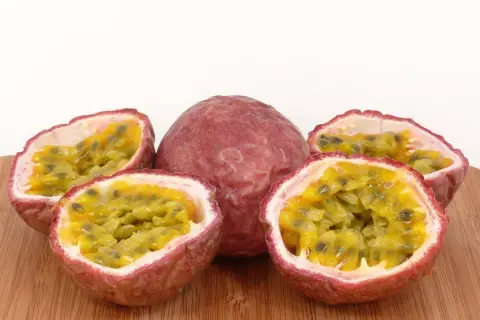 Ein ganzes und vier halbierte Passionsfrüchte liegen auf einem Holzbrett. Die Fruchtkerne sind saftig und gelb. Perfekt zum Passionsfrucht essen!