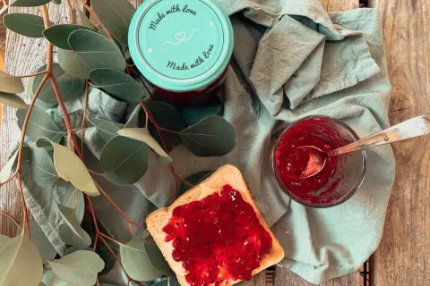 Glas mit Johannisbeermarmelade ohne Gelierzucker, daneben ein Toast mit Marmelade und ein Löffel.