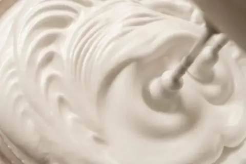 Sahne steif schlagen ohne Sahnesteif: Ein Handmixer formt cremige Wellen in der weißen Masse.