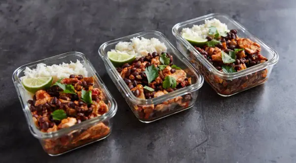 Drei Glasbehälter mit meal prep reis, Hähnchen, schwarzen Bohnen und Limettenspalten, garniert mit Petersilie.