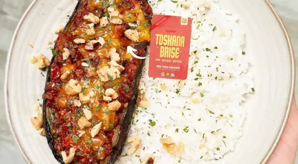 Gefüllte Aubergine mit einer würzigen Tofu-Bolognese-Mischung, garniert mit Walnüssen und Petersilie, serviert mit Reis.