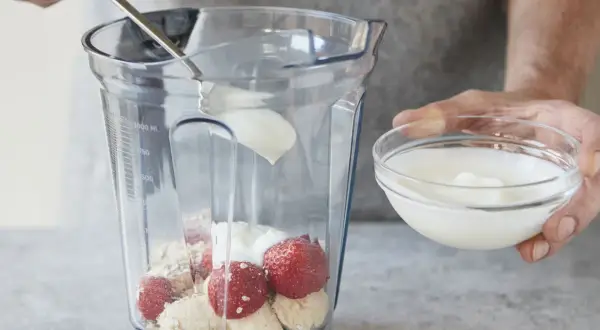 Joghurt wird mit Erdbeeren, Bananen und Haferflocken in einen Mixer gegeben. Ein gesunder Smoothie mit Haferflocken entsteht.