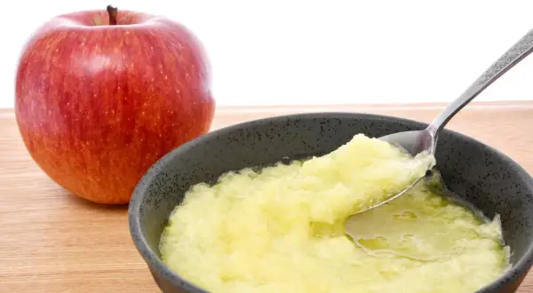 Ein roter Apfel neben einer Schüssel mit Apfelmus, ideal bei Magen-Darm-Beschwerden.