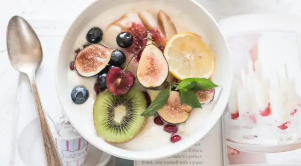 Schüssel mit Kokosjoghurt, garniert mit Feigen, Beeren, Kiwi und Zitrone. Ein gesundes Frühstück, das Lust auf mehr macht.