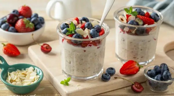 Zwei Gläser mit über Nacht eingeweichten Haferflocken, garniert mit frischen Beeren und Mandelsplittern. Ein gesunder Start in den Tag.