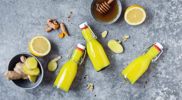 Zutaten für ein Ingwer Shot Rezept: frischer Ingwer, Zitrone, Honig und drei Flaschen des gelben Shots.