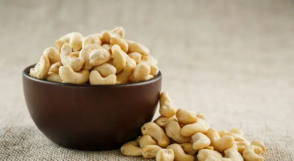 Schale mit Cashewkernen, die zeigen, wie gesund Cashewkerne sind. Ein paar Kerne sind daneben verstreut.