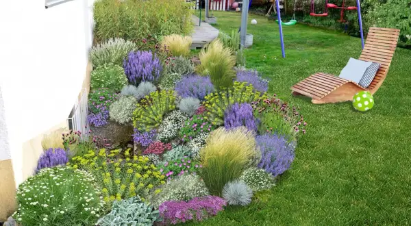 Ein üppig bepflanztes Blumenbeet mit Lavendel, Gräsern und vielen kleinen Blüten neben einem Haus. Perfekt, um **Pflanzsteine bepflanzen** zu lassen und einen schönen Garten zu gestalten.
