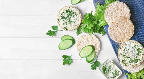 Reiswaffeln mit Frischkäse und Kräutern, Gurkenscheiben und Salat – eine leichte Mahlzeit, die zeigt, welche Reiswaffeln unbedenklich sind.