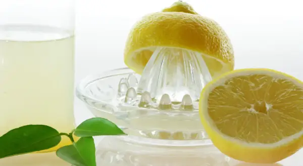 Frisch gepresster Zitronensaft in einem Glas, bereit zur Lagerung. Eine halbe Zitrone liegt auf einer Zitruspresse.