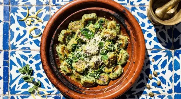 Spinat Ricotta Gnocchi, garniert mit Parmesan und Zitrone, serviert in einer Terrakotta-Schale auf blau-weißen Fliesen.