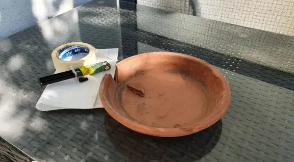 Zerbrochener Tontopf, Kleber und Klebeband liegen bereit, um den Schaden zu beheben.