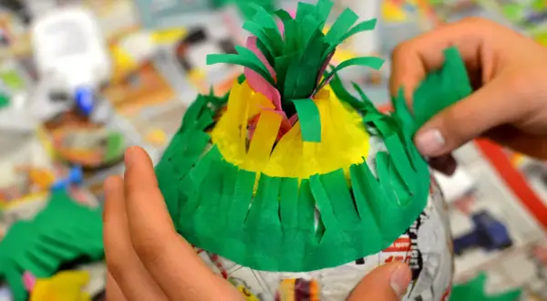 Hände basteln eine bunte Piñata. Mit grünem Krepppapier wird die Form verziert, um eine Piñata selber machen zu können.