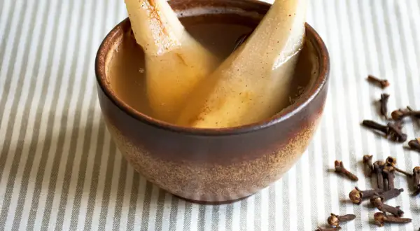 Zwei Birnenspalten in einer Schale mit Flüssigkeit, ein zuckerfreies Birnenkompott. Gewürznelken liegen daneben.