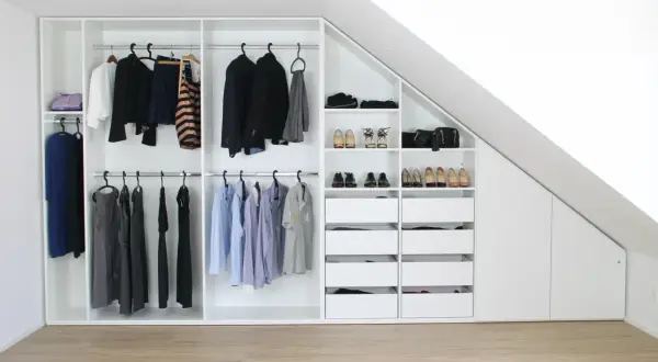 Ein maßgeschneiderter schrank selber bauen: weiße Kleiderschränke mit Kleiderstangen, Schubladen und Regalen, gefüllt mit Kleidung und Schuhen, unter einer Dachschräge.