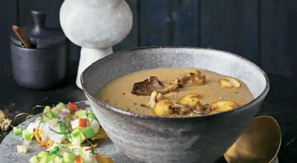 Herzhafte pilz suppe in einer rustikalen Schüssel, garniert mit gebratenen Pilzen. Daneben ein kleiner Salat mit Apfel und Kräutern.