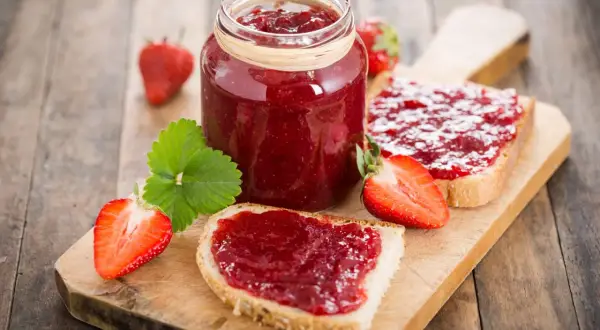 Ein Glas Erdbeermarmelade und Brotscheiben mit Marmelade. So einfach ist es, Marmelade zu machen!