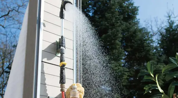 Gartendusche selber bauen: Eine Dusche mit Schlauchanschluss und Brausekopf sprüht Wasser vor einer Holzwand.