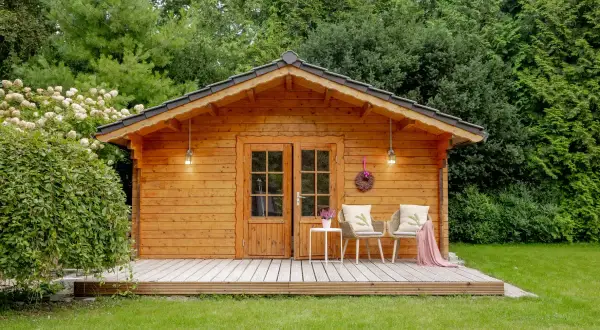 Ein gemütliches Gartenhaus, das man gut selber bauen kann, mit Veranda, zwei Stühlen und einer Tür.