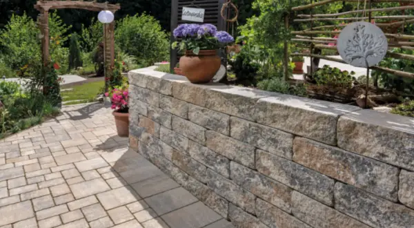 Eine stabile gartenmauer bauen aus Natursteinblöcken, die den Gartenbereich stilvoll abgrenzt und mit Blumen und Pflanzen dekoriert ist.