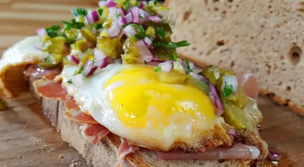 Ein **strammer Max vegetarisch** mit Spiegelei, Schinken, Gewürzgurken und Zwiebeln auf rustikalem Brot.