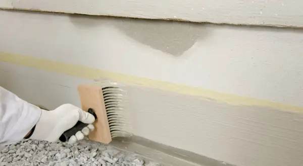 Mit einem Pinsel wird der Sockel verputzt. Klebeband schützt die Wand.
