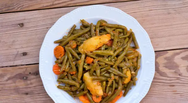 Ein Teller mit einem köstlichen Fasolakia Rezept, das grüne Bohnen, Kartoffeln und Karotten in einer würzigen Sauce zeigt.