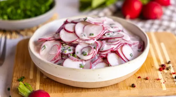 Frischer radieschensalat mit joghurt und schnittlauch, garniert mit pfefferkörnern.
