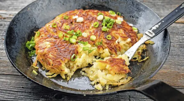 Herzhaft gebratene Kartoffelpuffer, perfekt für Meal Prep Kartoffeln, garniert mit Frühlingszwiebeln in einer Gusseisenpfanne.