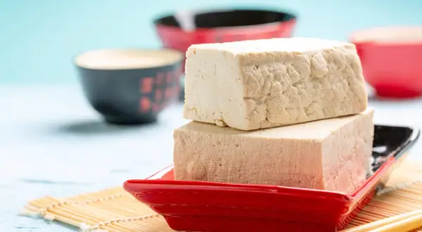 Zwei Blöcke Tofu auf einem roten Teller, bereit zum Genuss. Ja, man kann Tofu roh essen, er ist vielseitig!