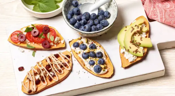 Brotalternativen: Süßkartoffelscheiben belegt mit Tomaten, Feta, Oliven, Blaubeeren, Pistazien, Avocado und Leinsamen.