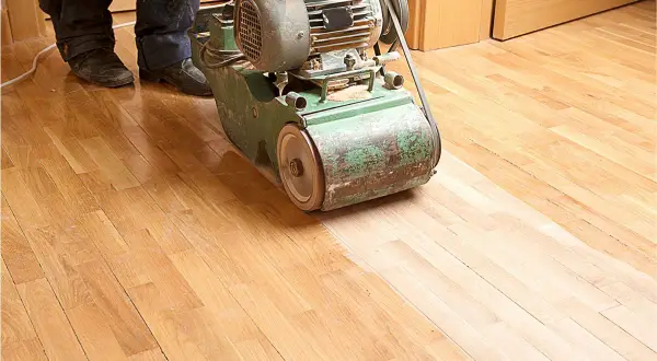 Ein Handwerker bearbeitet mit einer Schleifmaschine einen Holzboden. Das Parkett abschleifen erweckt den alten Boden zu neuem Glanz.