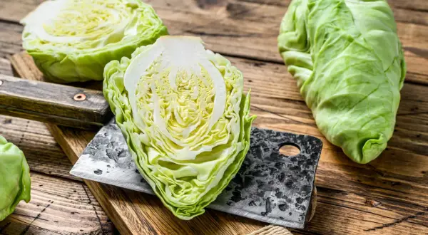 Frischer Spitzkohl, halbiert und auf einem Holzbrett mit einem Hackmesser. Perfekt, um Spitzkohl roh zu essen für einen knackigen Salat.
