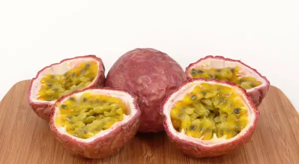 Ein ganzes und vier halbierte Passionsfrüchte liegen auf einem Holzbrett. Die Fruchtkerne sind saftig und gelb. Perfekt zum Passionsfrucht essen!