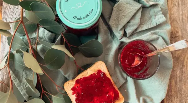 Glas mit Johannisbeermarmelade ohne Gelierzucker, daneben ein Toast mit Marmelade und ein Löffel.