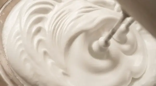 Sahne steif schlagen ohne Sahnesteif: Ein Handmixer formt cremige Wellen in der weißen Masse.