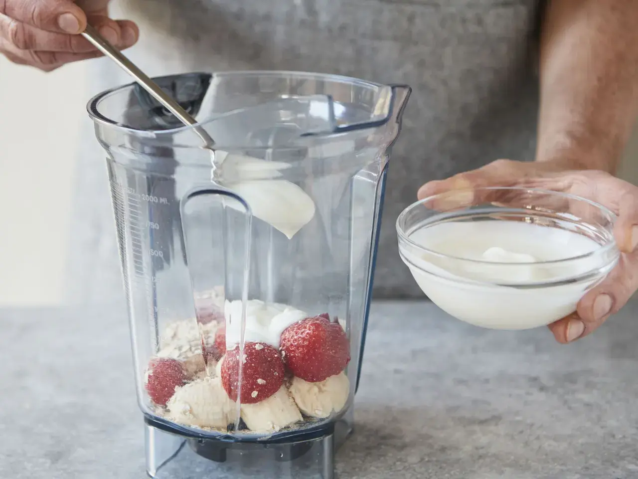 Joghurt wird mit Erdbeeren, Bananen und Haferflocken in einen Mixer gegeben. Ein gesunder Smoothie mit Haferflocken entsteht.
