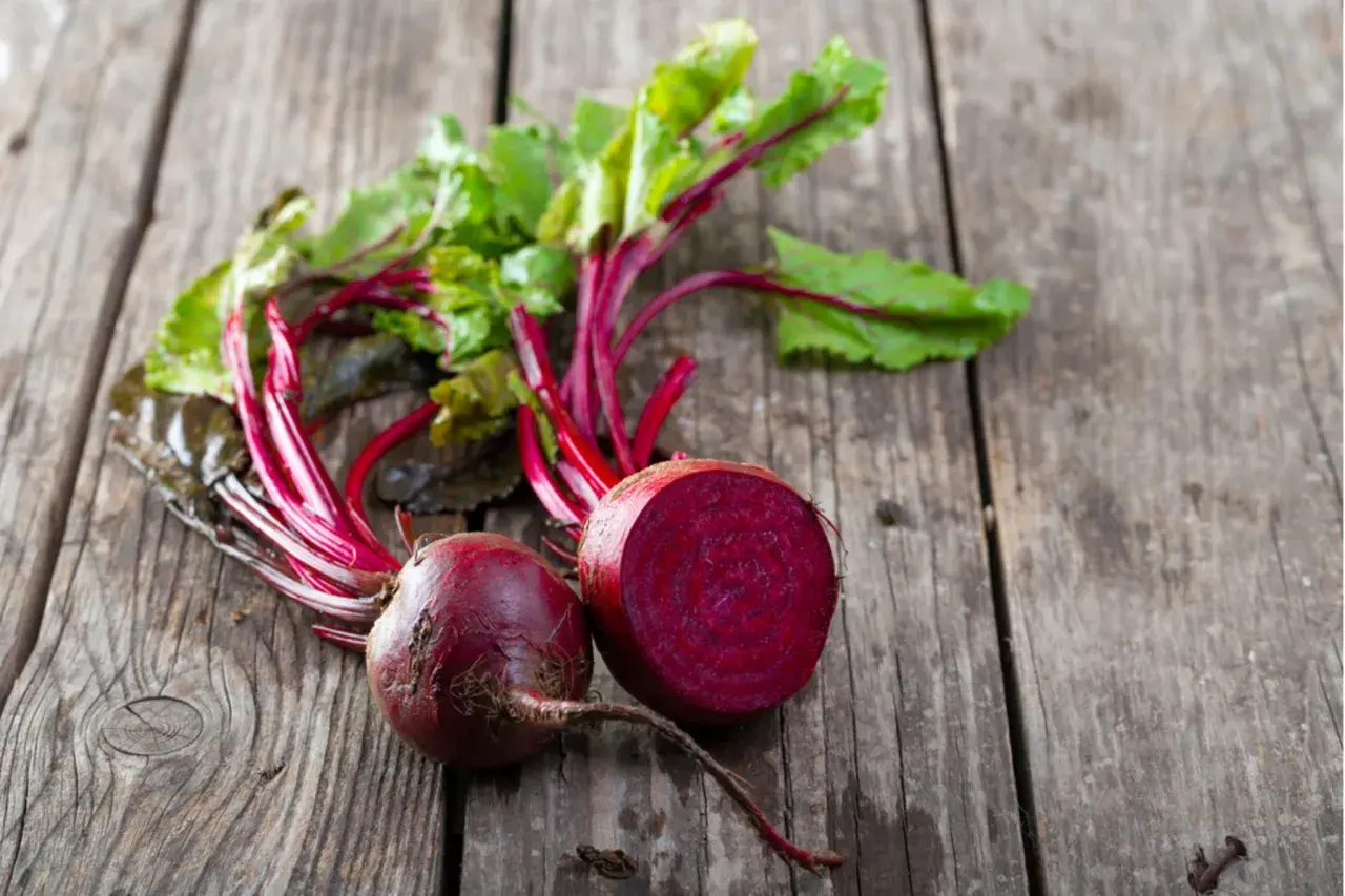 Zwei frische rote Bete, eine davon halbiert, liegen auf rustikalem Holz. Perfekt, um rote Beete roh zu essen und die gesunden Nährstoffe zu genießen.