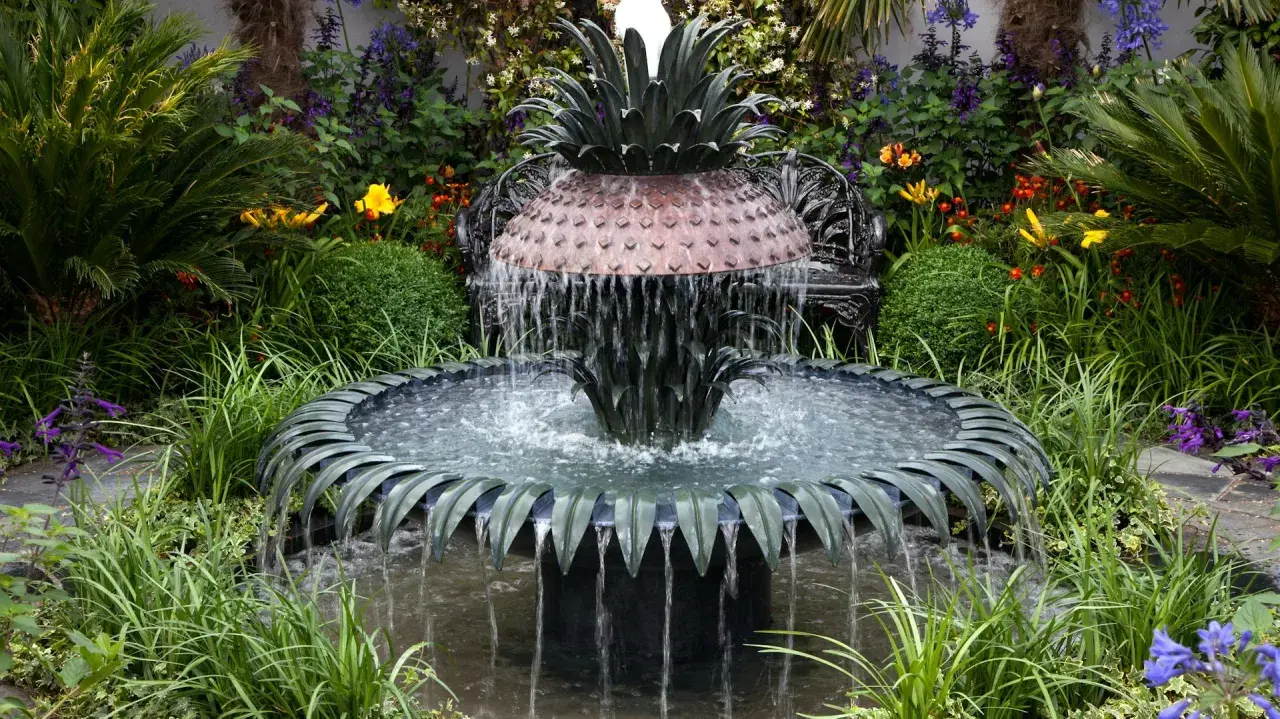 Ein kunstvoller Gartenbrunnen im Ananas-Design, der zum **gartenbrunnen selber bauen** inspiriert. Umgeben von üppiger Vegetation und bunten Blumen.