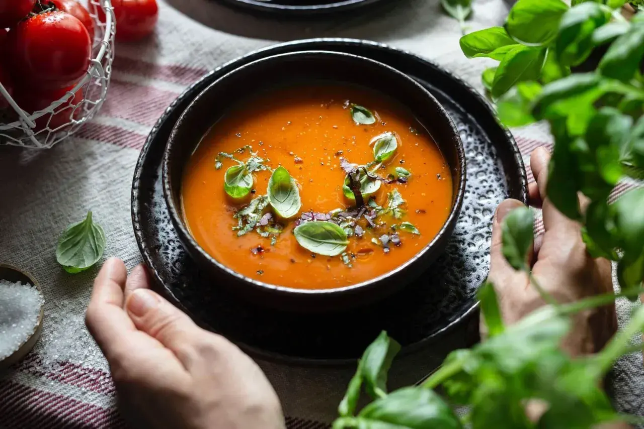 Schüssel mit leckerer Tomatensuppe, garniert mit Basilikum. Ein Korb mit frischen Tomaten und Salz daneben. Perfekt für ein Tomatensuppe Rezept mit frischen Tomaten.