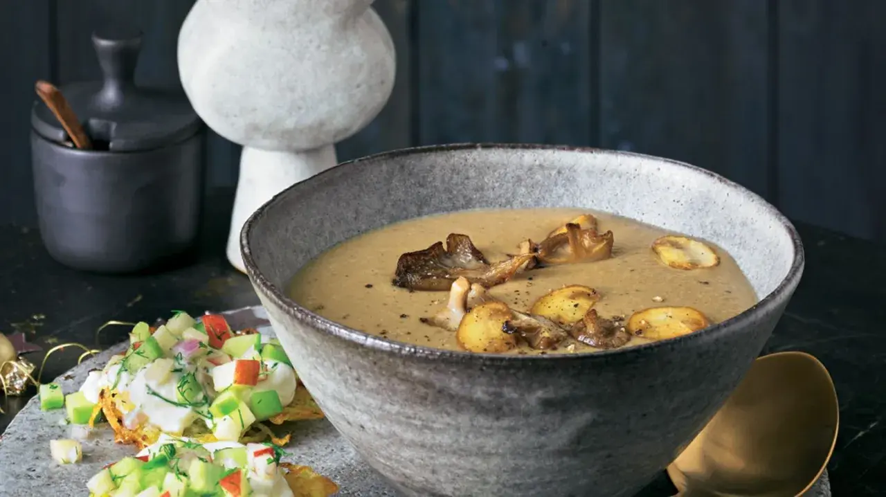 Herzhafte pilz suppe in einer rustikalen Schüssel, garniert mit gebratenen Pilzen. Daneben ein kleiner Salat mit Apfel und Kräutern.