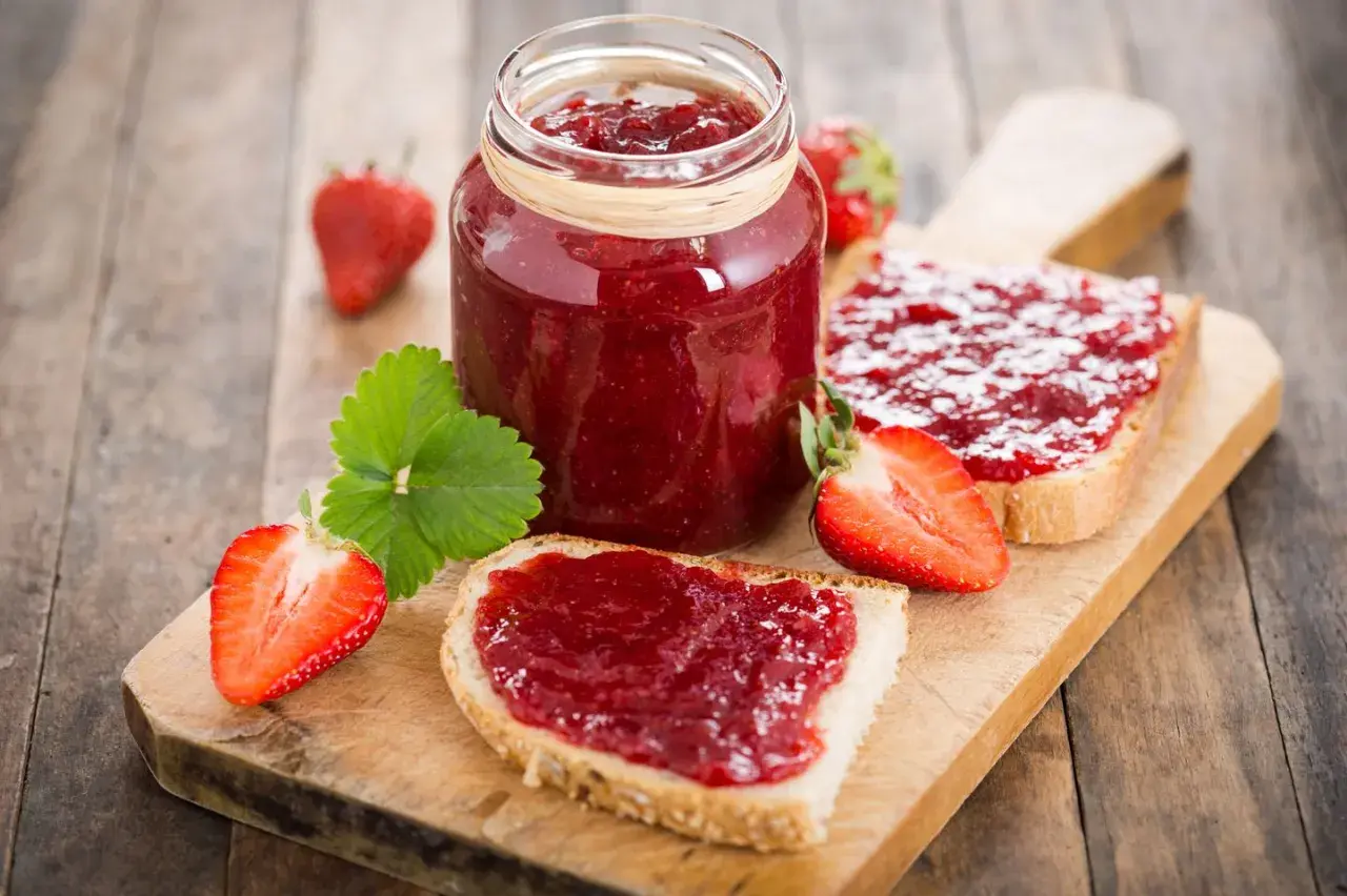 Ein Glas Erdbeermarmelade und Brotscheiben mit Marmelade. So einfach ist es, Marmelade zu machen!