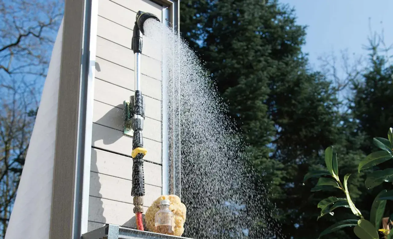 Gartendusche selber bauen: Eine Dusche mit Schlauchanschluss und Brausekopf sprüht Wasser vor einer Holzwand.