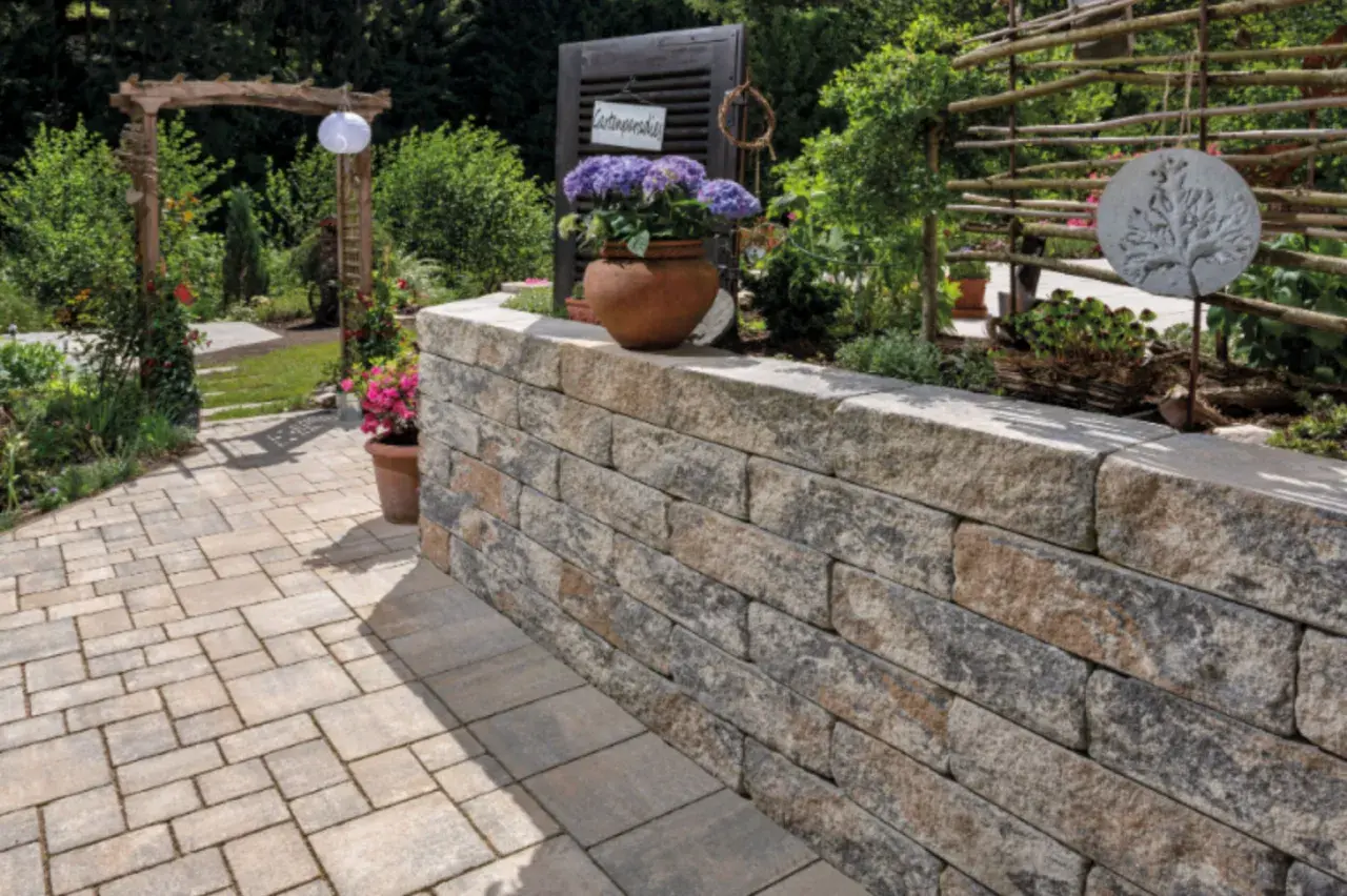 Eine stabile gartenmauer bauen aus Natursteinblöcken, die den Gartenbereich stilvoll abgrenzt und mit Blumen und Pflanzen dekoriert ist.