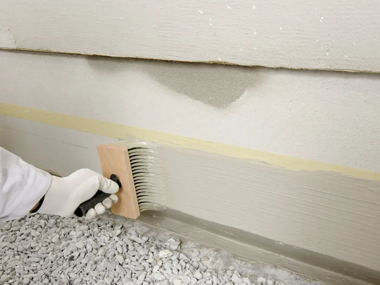 Mit einem Pinsel wird der Sockel verputzt. Klebeband schützt die Wand.